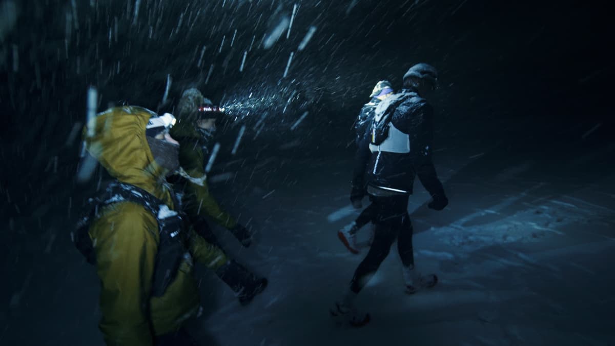 Runners battling through a snowstorm at night with headlamps